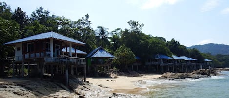 Una propiedad frente a la playa con varias casas sobre pilotes, una playa de arena y un litoral rocoso.