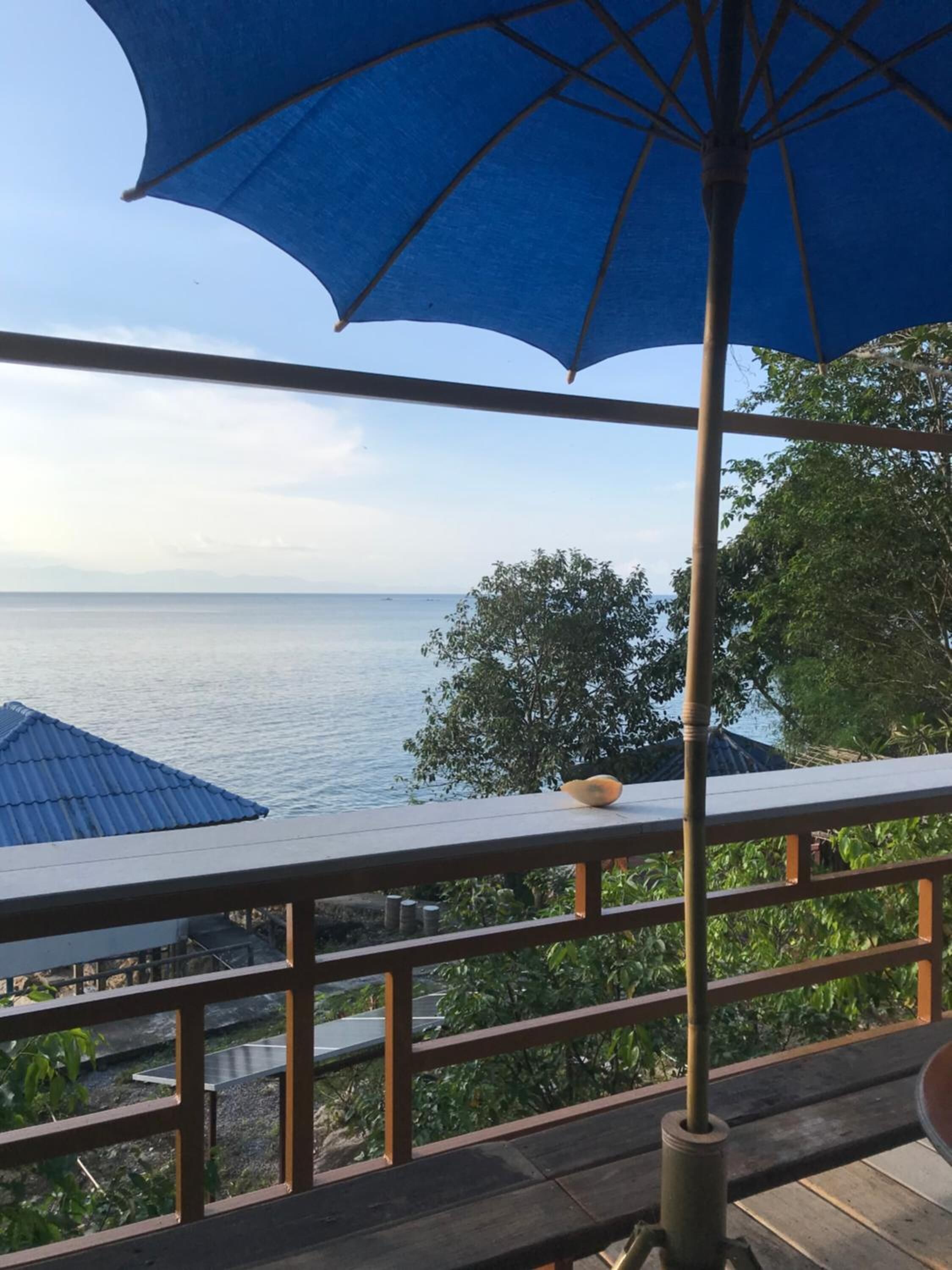 A balcony with a view of the sea, a blue umbrella, and a wooden railing.
