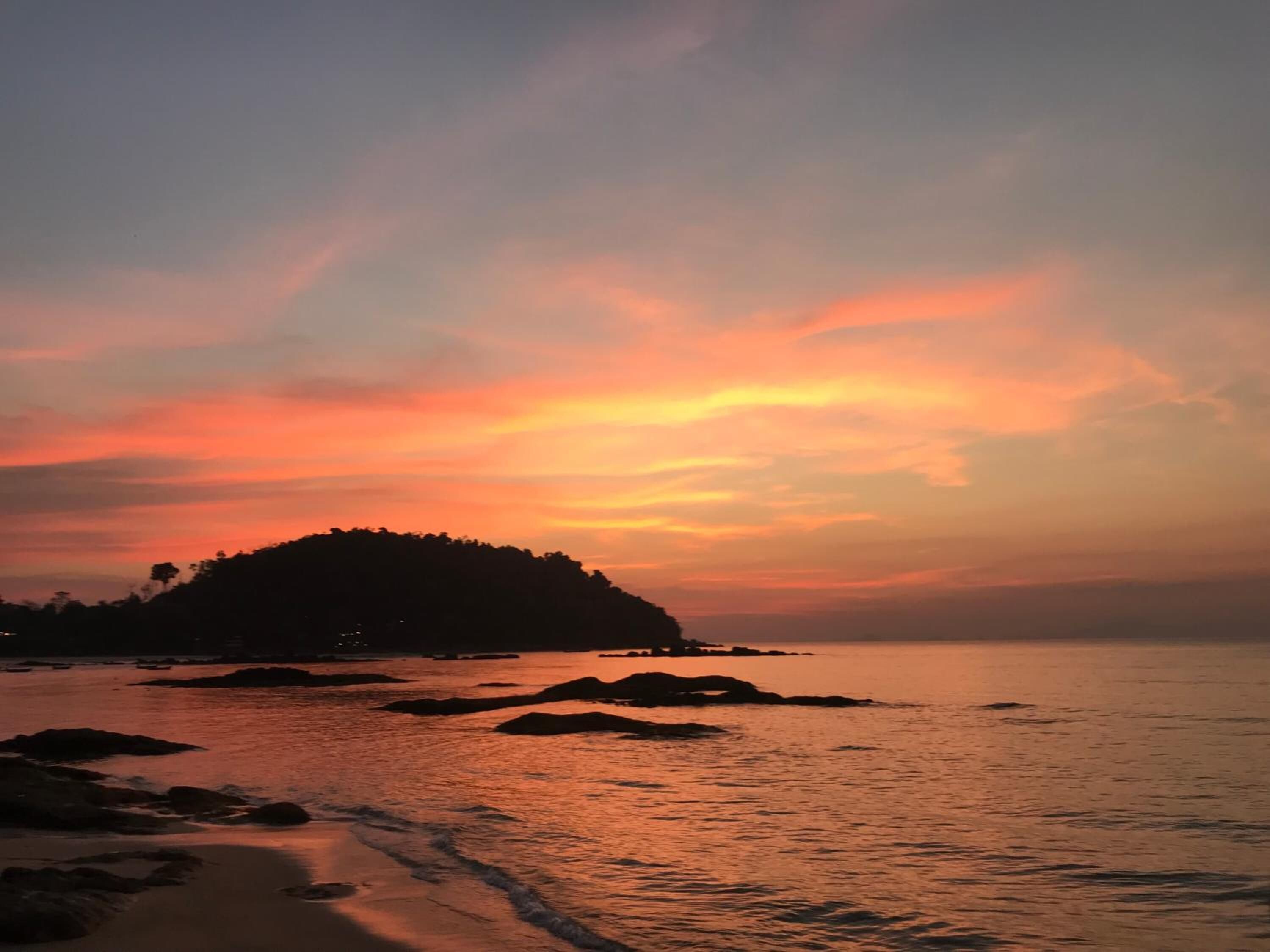 A beach with a rocky shoreline and a hill in the background during sunset.