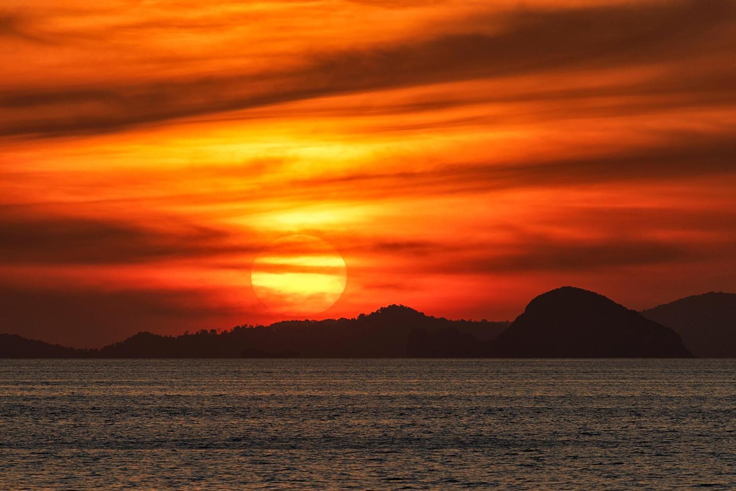 Un atardecer sobre el agua, con siluetas de montañas al fondo.