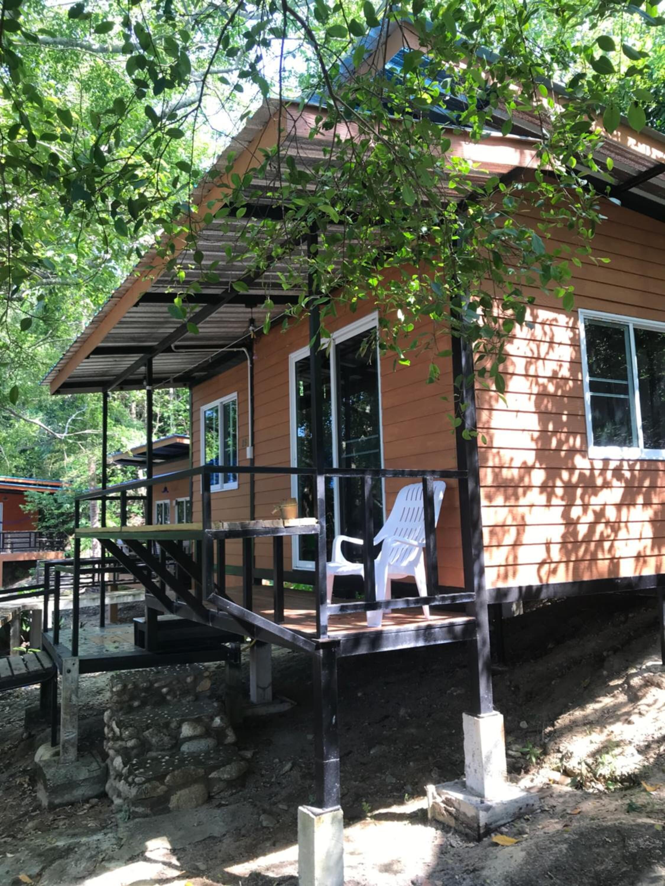 Une cabane en bois avec une véranda, une chaise en plastique blanche et un escalier menant à l’entrée.