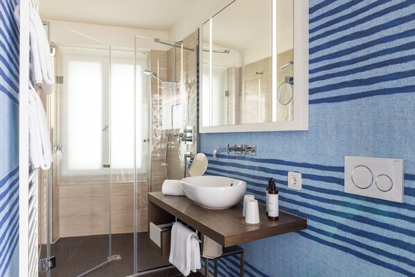 A modern bathroom with a glass-enclosed shower, a large mirror, and a wooden vanity with a vessel sink. - Hotel Stein - Adults Only (Salzburg)