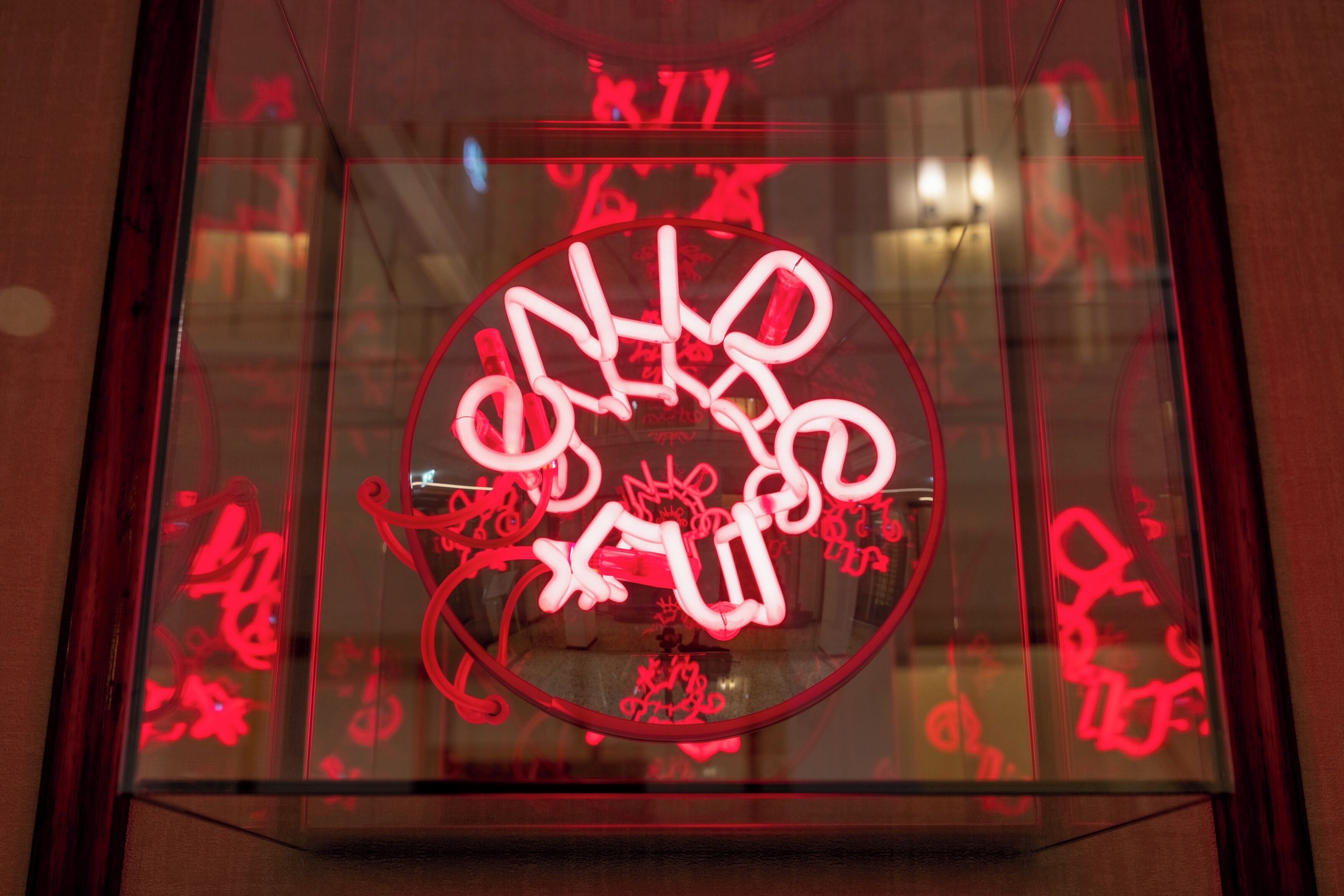 A neon sign with abstract designs inside a glass enclosure.