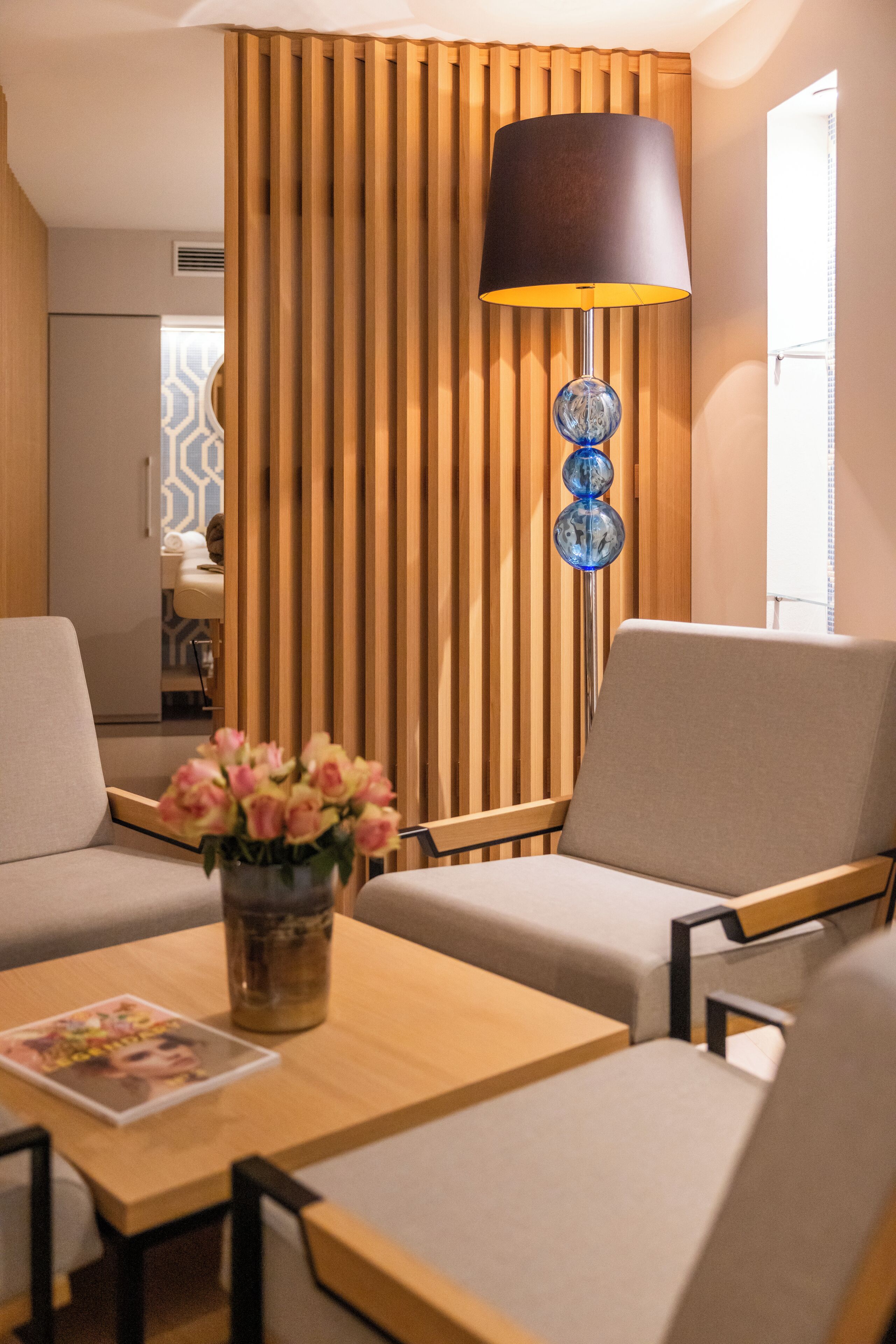 A modern room with a wooden slat partition, a table with a vase of flowers, and two armchairs.