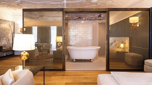 Une chambre d’hôtel moderne dotée d’une baignoire sur pieds classique, d’un grand miroir et d’un coin salon confortable.