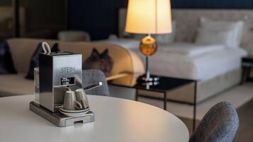 A hotel room with a bed, a lamp, a coffee machine, and a sofa.