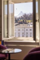 Una stanza con vista su montagne ed edifici attraverso una finestra aperta.