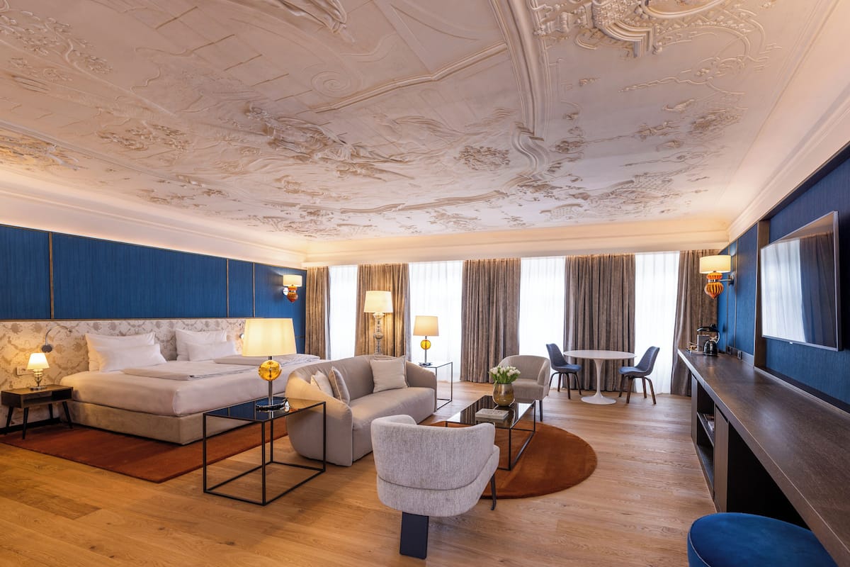A spacious hotel room with a large bed, a sitting area with a coffee table, a dining table, and a TV.