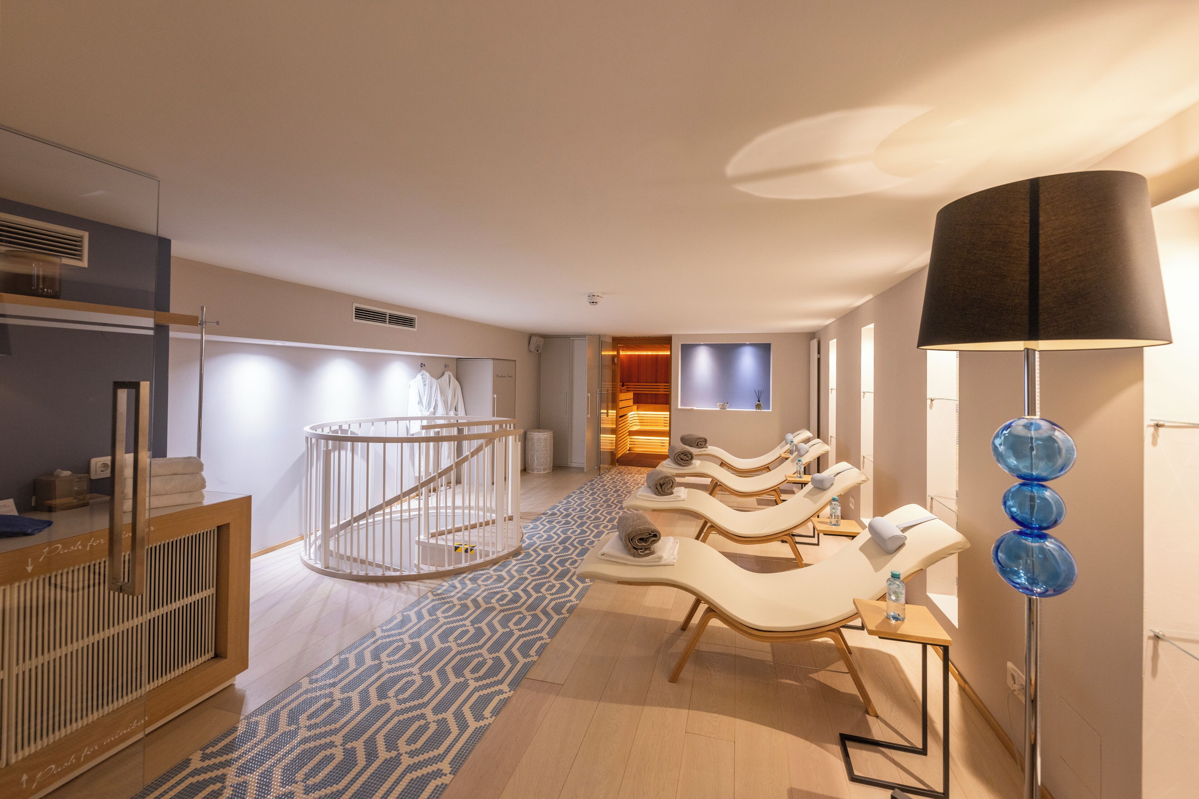 A modern spa room with a reception desk, a baby changing area, and several massage chairs.