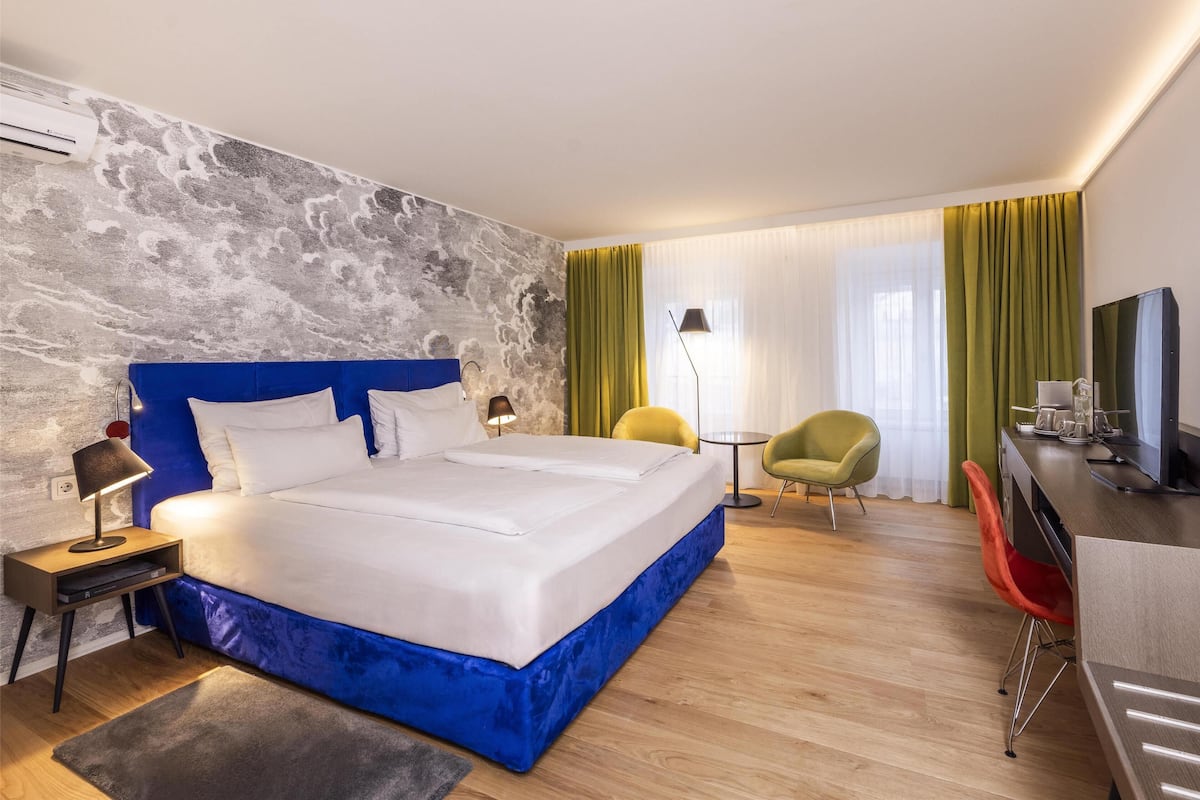 A modern hotel room with a large bed, a desk, a chair, and a television.