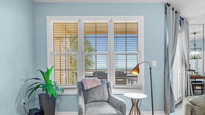A room with a large window, a grey armchair, a small table, a floor lamp, and a potted plant. - 202E - Newly Remodeled! (Gulf Shores)