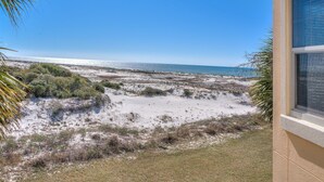 A coastal view with a sandy beach, sparse vegetation, and a clear blue sky. - 202E - Newly Remodeled! (Gulf Shores)