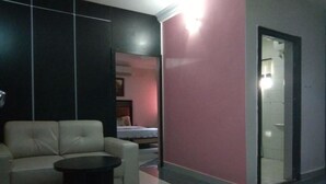 A hotel lobby with a sofa, a small round table, a pink wall, and a glass door leading to another room. - Jesuit Continental Suites (Abuja)