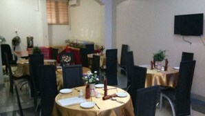 A conference room with round tables, black chairs, and a television mounted on the wall. - Jesuit Continental Suites (Abuja)