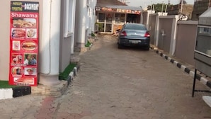 A paved walkway leading to a building with a signboard advertising food items like shawarma, burgers, and ice cream. - Jesuit Continental Suites (Abuja)