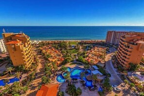 Ein Resort mit mehreren Gebäuden, einem zentralen Poolbereich und Blick auf den Ozean.
