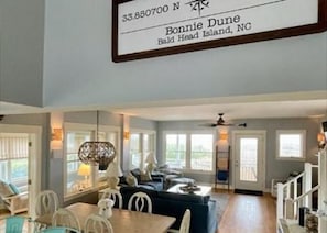 A spacious living room with a large window, a dining area with a table and chairs, and a ceiling fan.