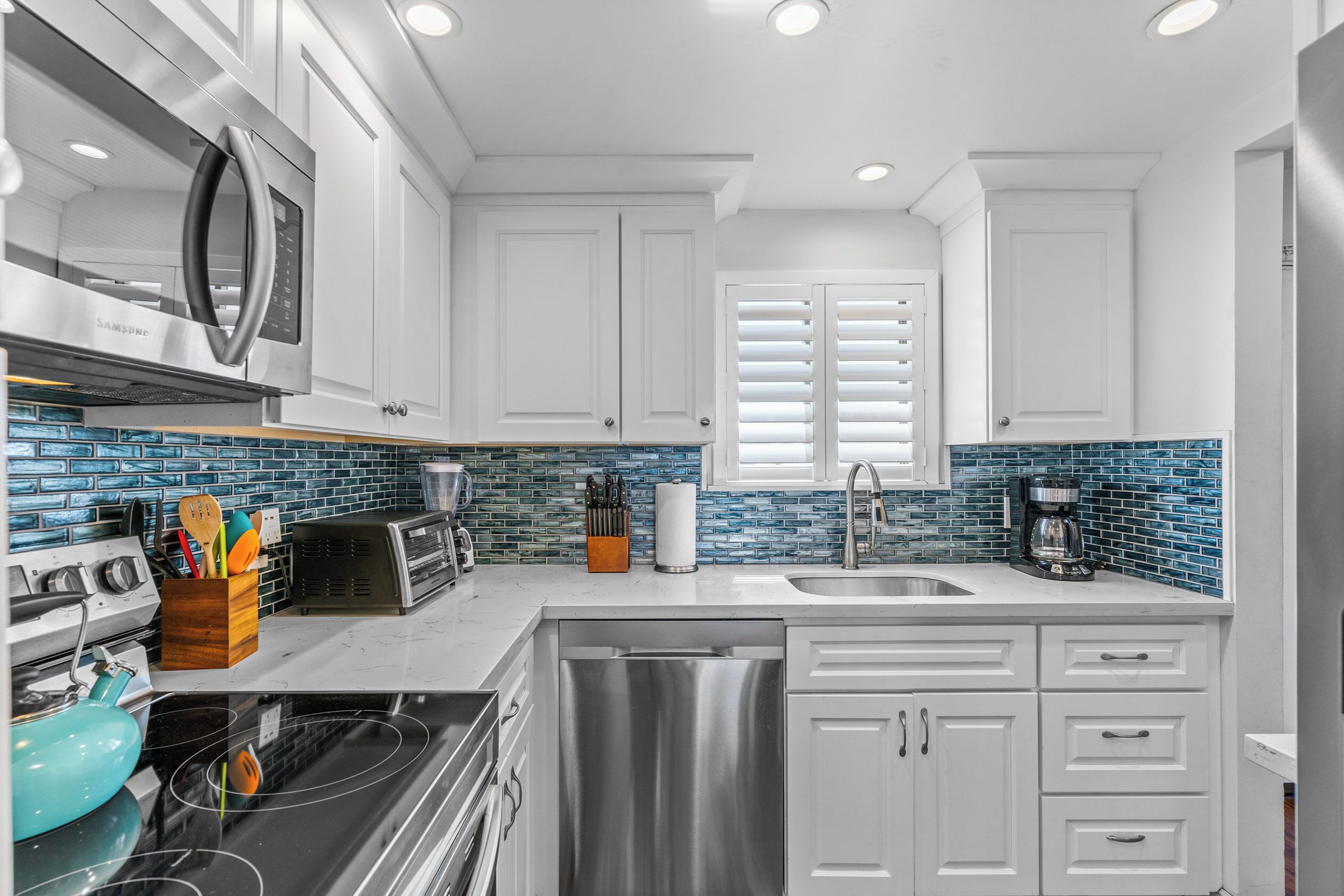 A modern kitchen with white cabinets, a stainless steel dishwasher, a microwave, and a toaster.