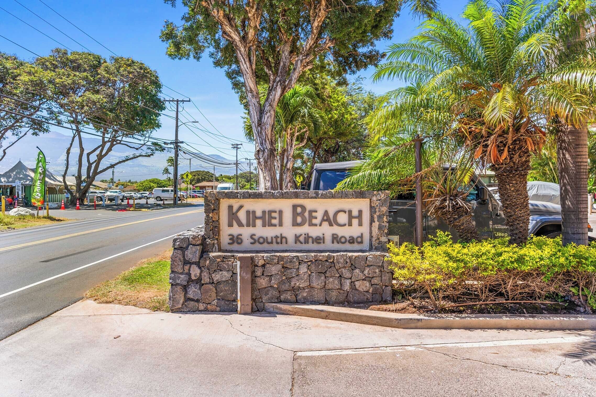 A street sign for Kihei Beach at 36 South Kihei Road, surrounded by palm trees and a clear sky.