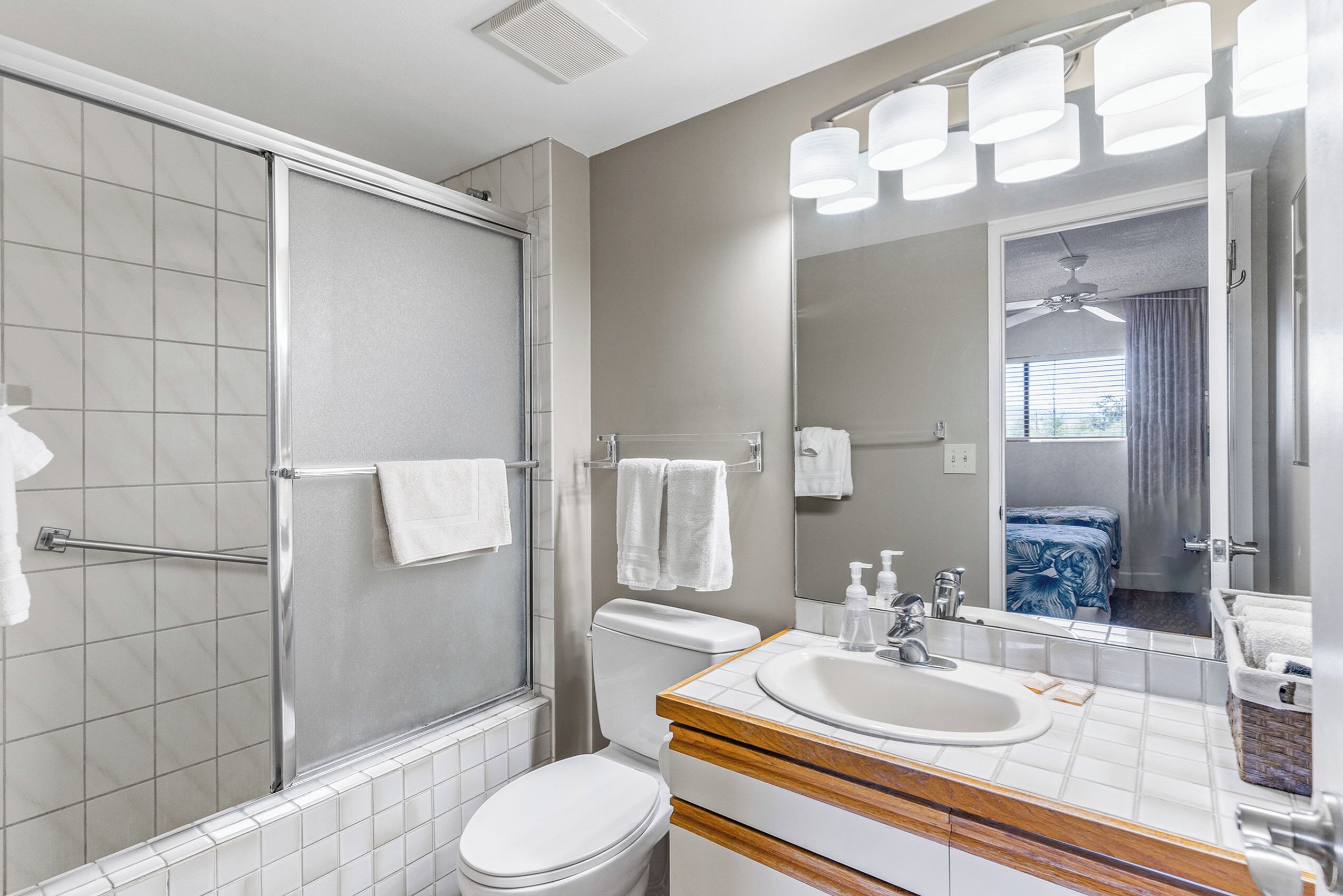 A bathroom with a shower, toilet, sink, and a large mirror.