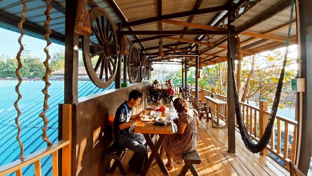Une terrasse en bois avec des tables et des chaises, de grandes roues fixées au plafond et une vue sur l’eau.