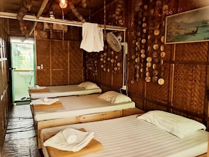 Una habitación rústica con tres camas de madera, un ventilador y una pared decorada con objetos de madera.