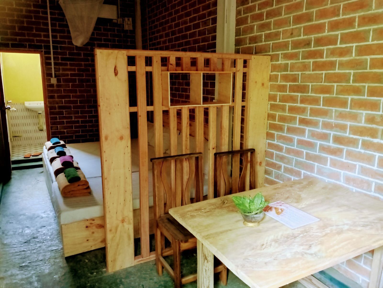 A room with a wooden partition, a table with a plant, and a bench with towels.