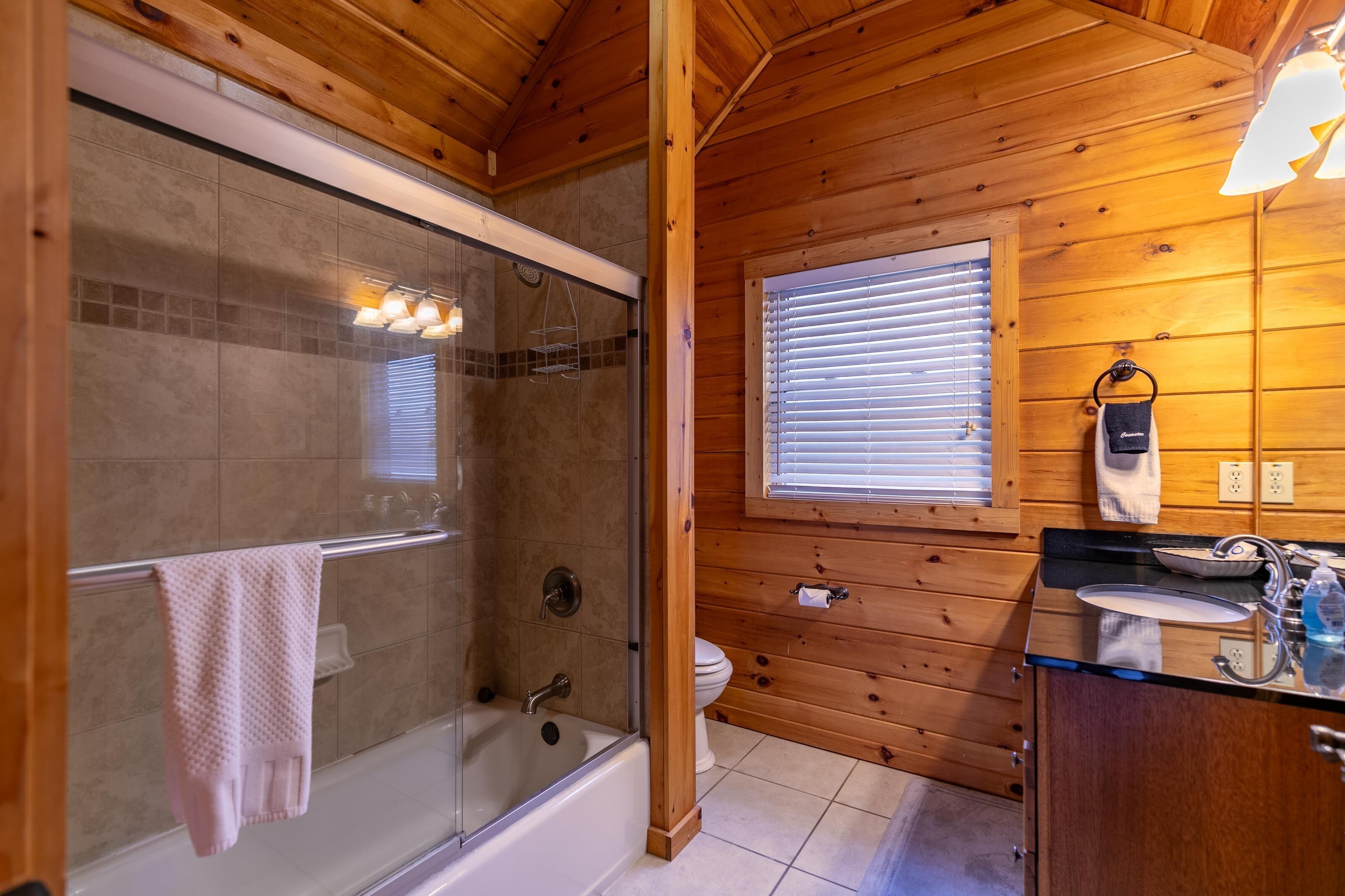 A wooden cabin bathroom with a glass-enclosed shower, a toilet, and a sink with a mirror.