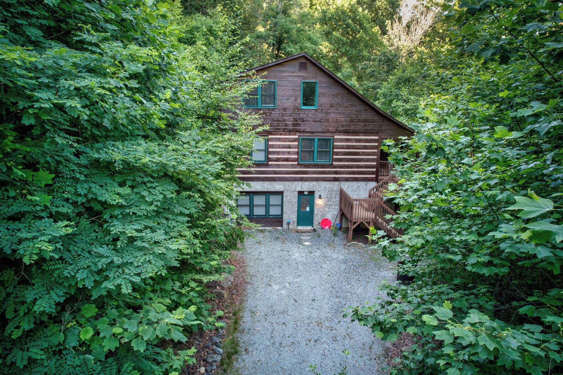 Una cabaña rodeada de un bosque denso, con un camino de grava que lleva a la entrada.