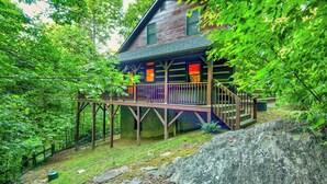 A cabin with a wooden deck, surrounded by dense forest.