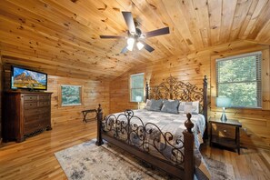 A wooden cabin bedroom with a bed, dresser, ceiling fan, and a television on the wall. - Uncle Johns Cabin | Valle Crucis | Hot Tub, Game Room, Fireplace (Vilas)