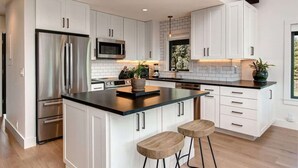 A modern kitchen with white cabinetry, stainless steel appliances, a black countertop island, and bar stools. - Abode at Rendezvous, private entrance, large deck (Teton Village)