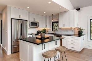 Una cocina moderna con armarios blancos, electrodomésticos de acero inoxidable, una isla con encimera negra y taburetes de bar.