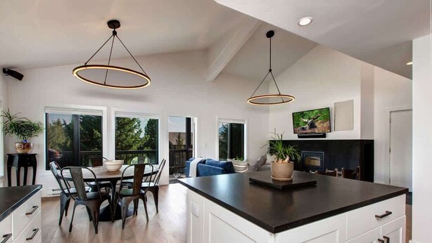 A modern kitchen with a large island, pendant lighting, and a dining area with a table and chairs. - Abode at Rendezvous, private entrance, large deck (Teton Village)