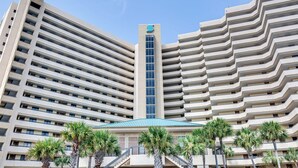 A high-rise hotel with a distinctive zigzag facade, multiple balconies, and a central entrance with a blue roof. - 2 BR Condo! Awesome Views! 14th floor!  Resort on Sand! Heart of Destin! (Destin)