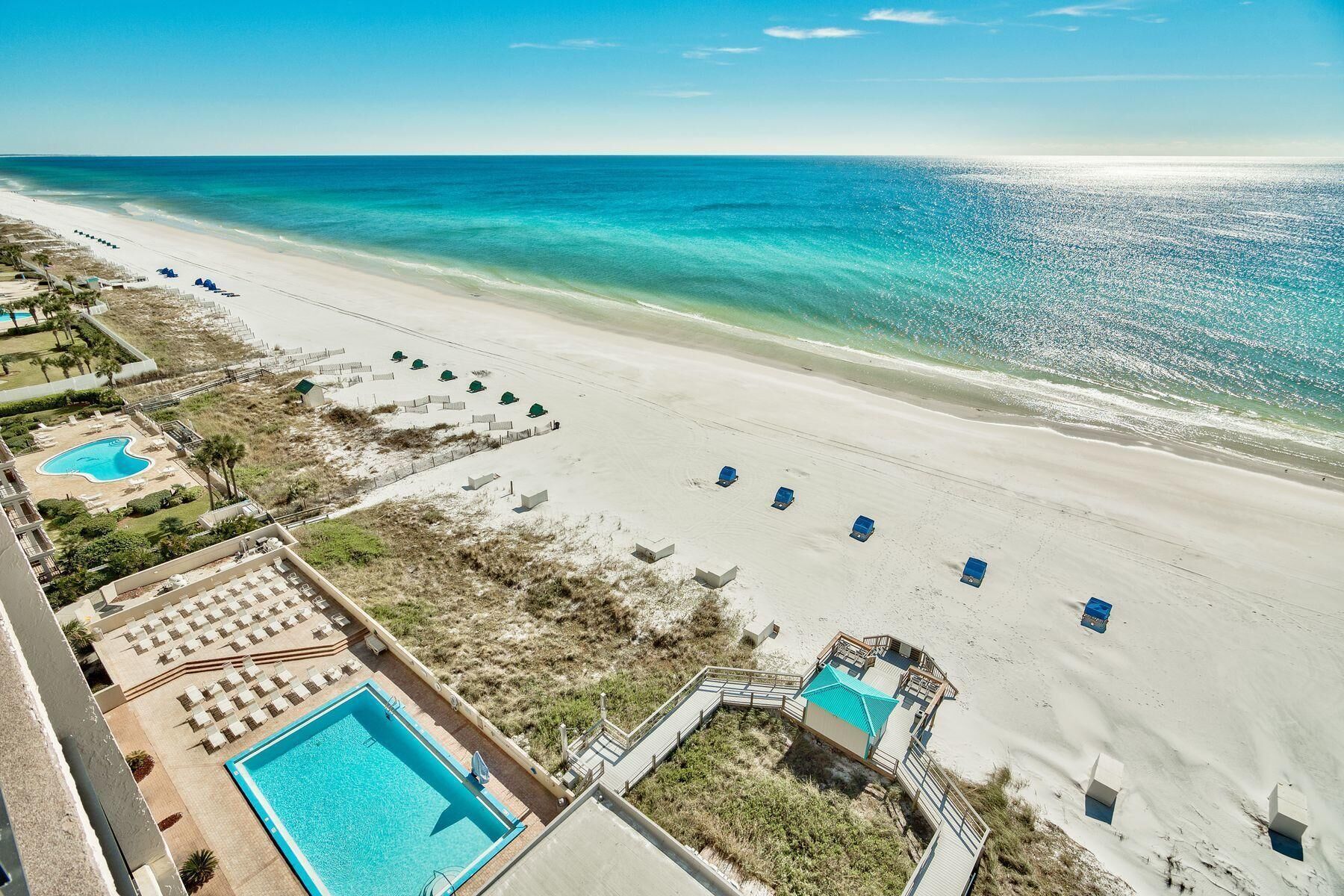 A beach resort with a swimming pool, beach umbrellas, and a lifeguard tower.