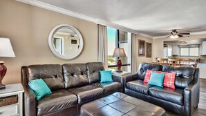 A living room with a brown leather sectional sofa, a matching ottoman, and a round mirror on the wall. - 2 BR Condo! Awesome Views! 14th floor!  Resort on Sand! Heart of Destin! (Destin)
