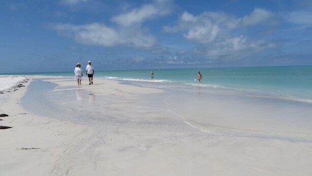 Ein Strand mit weißem Sand und klarem türkisblauem Wasser.