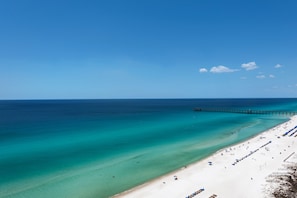 A beach with a pier extending into the ocean, a sandy shore with beach umbrellas, and clear blue water. - 1703 - 3 Bedroom 3 Bath. Master Bedroom on the Gulf (Panama City Beach)