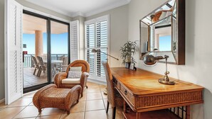 Ein Zimmer mit Schreibtisch aus Holz, Korbstühlen, einem großen Spiegel und Blick auf den Balkon.
