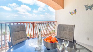 Ein Balkon mit einem Glastisch, zwei gepolsterten Stühlen, einer Flasche, einer Schale Orangen und zwei Gläsern Weißwein.