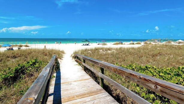 A wooden boardwalk leading to a beach with clear skies.