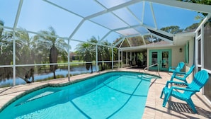 A clear pool with a covered patio area, outdoor chairs, and a view of a lake.