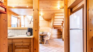 Interno di una baita in legno con cucina, zona pranzo e una scala.