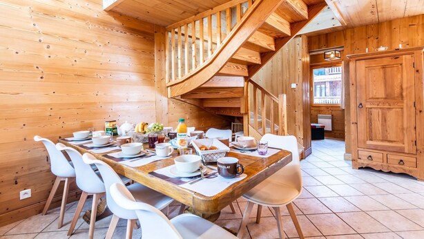 Interno di una baita in legno con zona pranzo, scala a chiocciola e cucina.