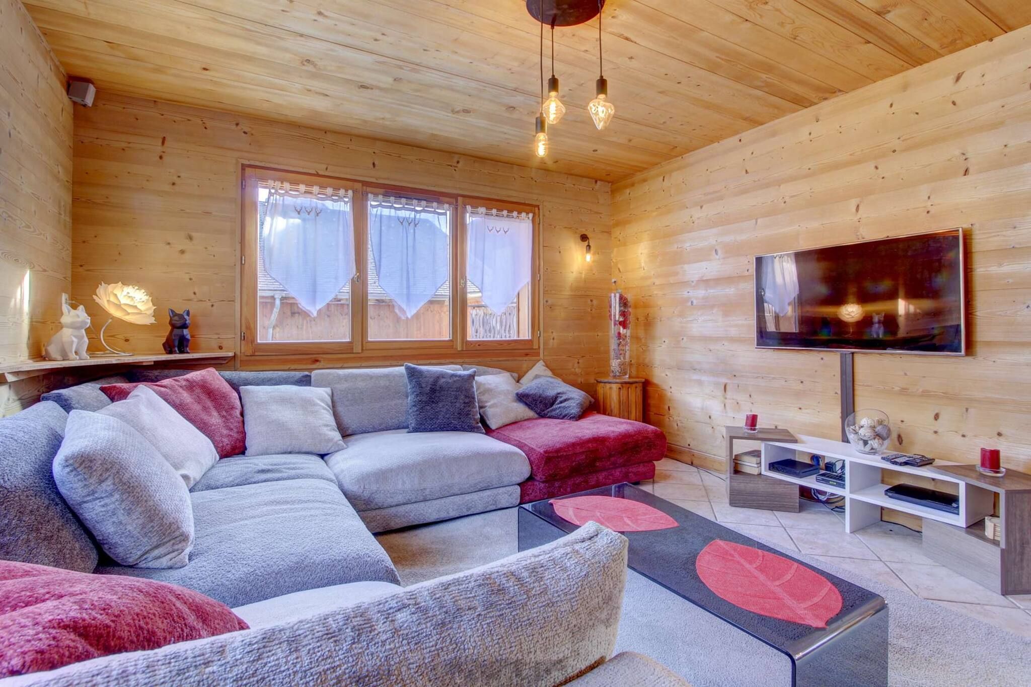 A cozy cabin interior with a sectional sofa, a flat-screen TV, and a wooden ceiling.