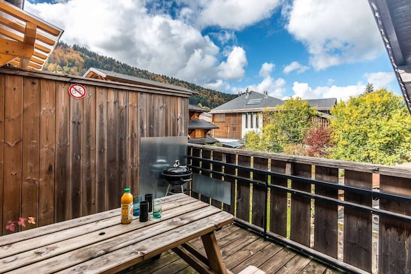 A wooden deck with a picnic table, a grill, and a view of a mountain and buildings.