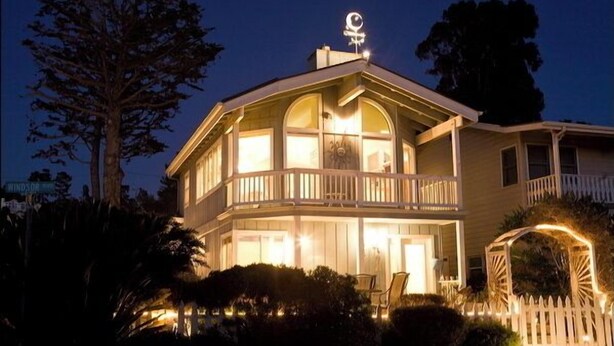 Een huis met twee verdiepingen, een balkon en een veranda, omringd door bomen en een witte hekwerk.