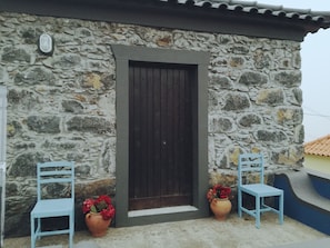 A stone building with a dark wooden door, two blue chairs, and two terracotta pots with red flowers. - My Favorite Spot in Madeira (São Vicente)