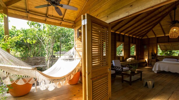 A wooden cabin with a hammock, a bed, a table, and a chair. - BAYLEAF: The Perfect Hideaway near secluded beach (Hellene)